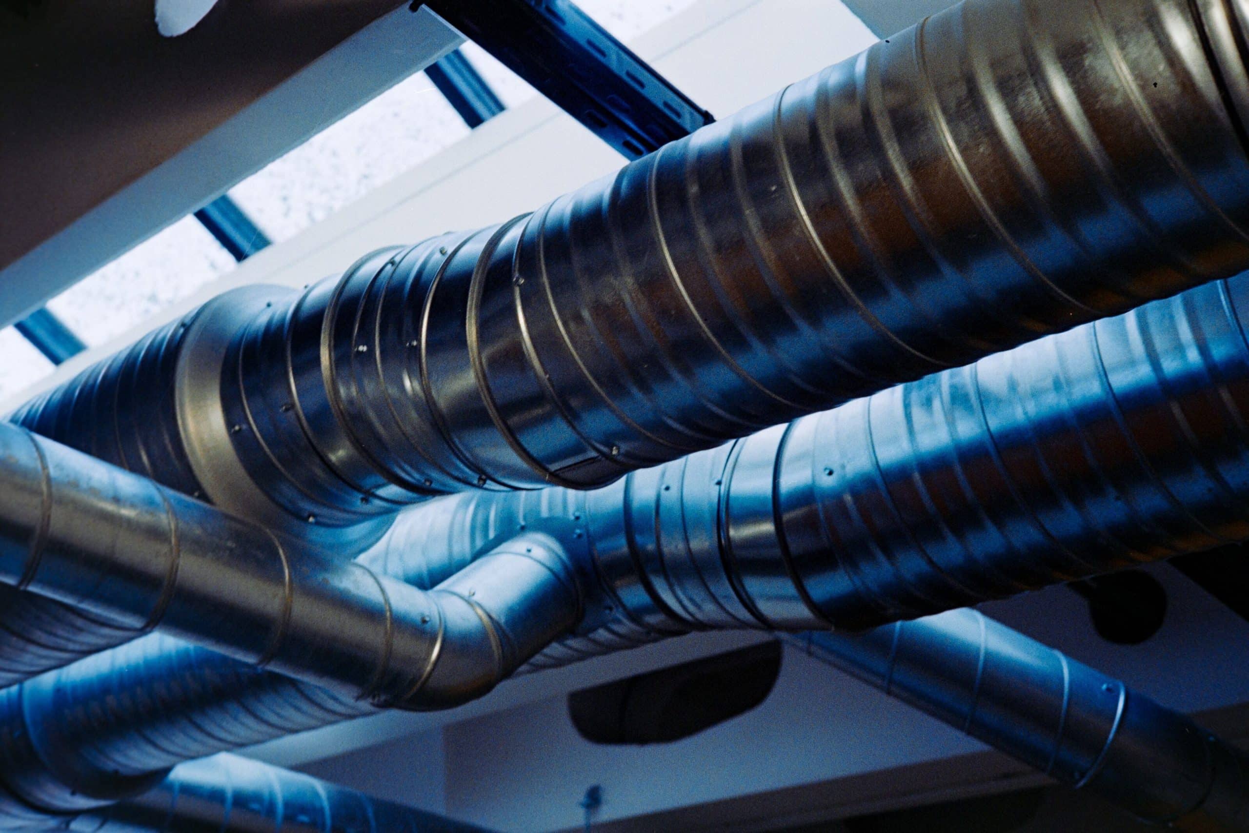 Galvanized metal ventilation ducts and branch connections above a building ceiling.