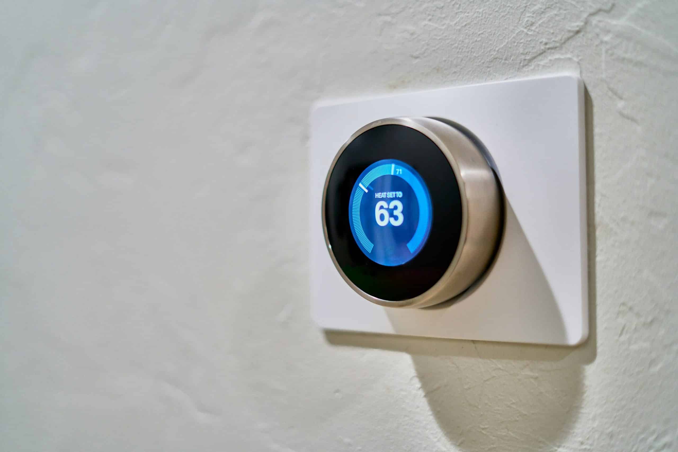 Close-up of a round wall-mounted thermostat with a blue display set to 63 degrees Fahrenheit.